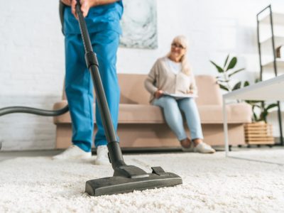 cropped shot of man using vacuum cleaner while senior woman sitting on sofa